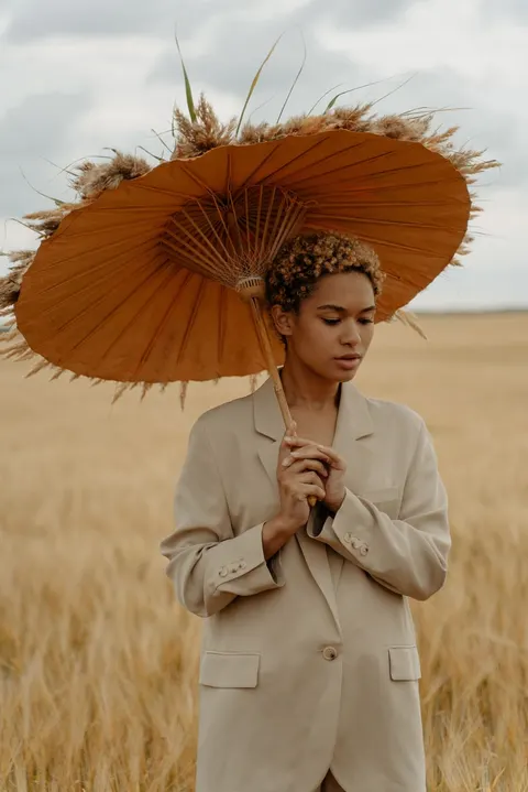 A model under a straw parasol, hands clasped