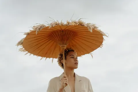 A model's face under a straw parasol against a pale sky
