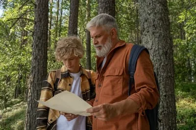 A man and a boy reading a paper map among the pines